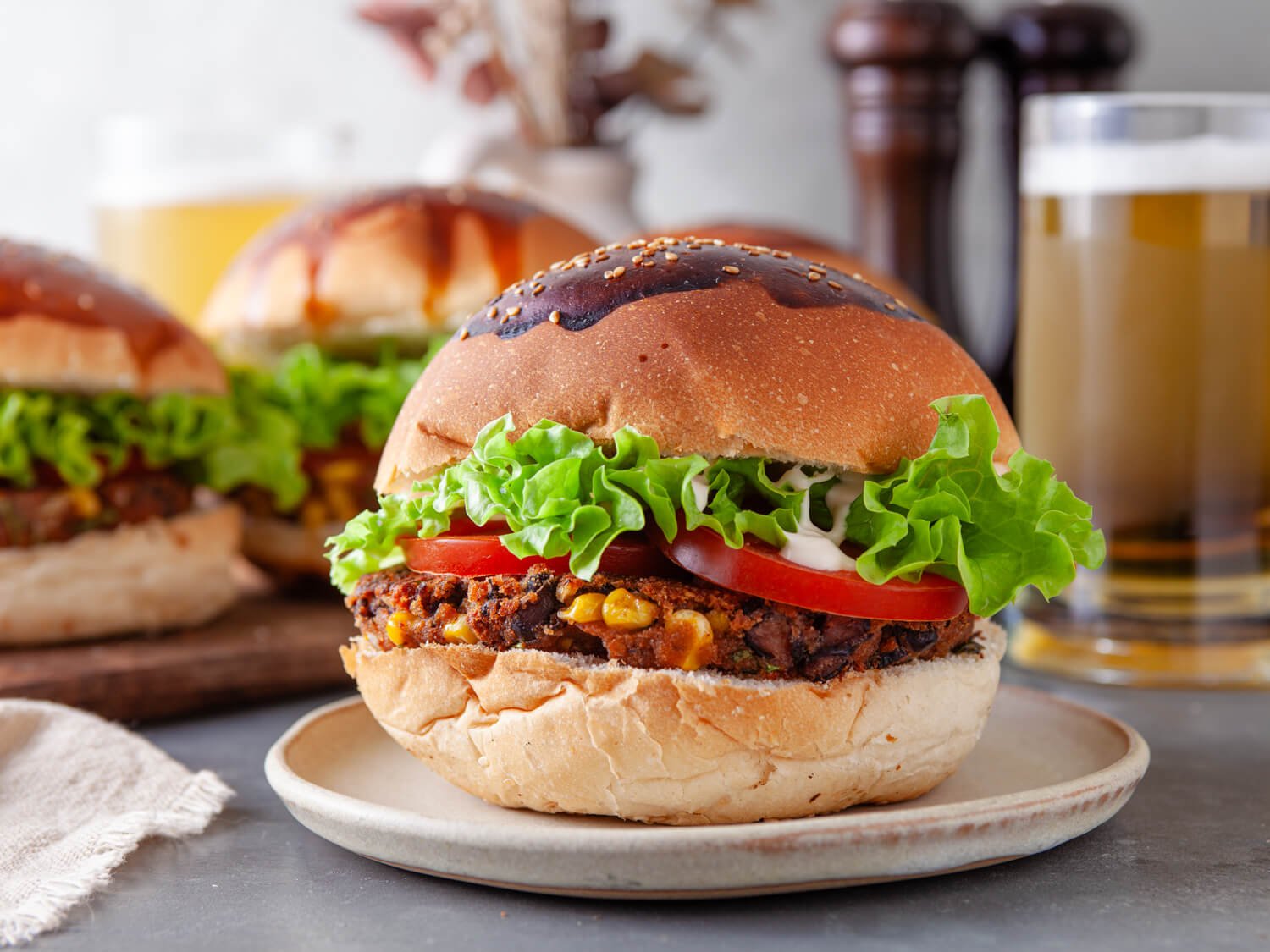 A close-up of a black bean veggie burger on a plate, with more burgers and a glass of beer in the background