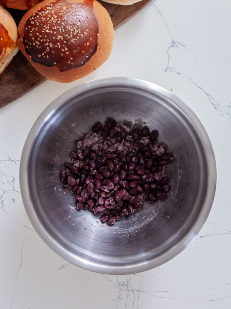 Mashed black beans in a large metal mixing bowl