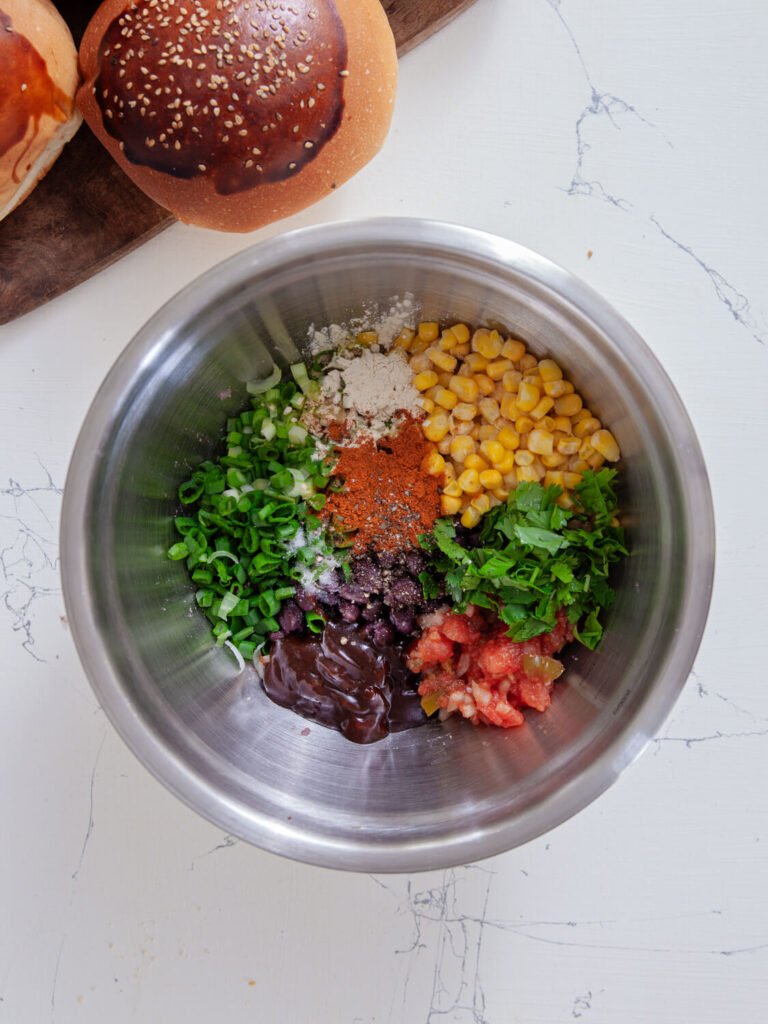 A bowl filled with black beans, corn, chopped green onions, salsa, fresh cilantro, barbecue sauce, spices, flour, and seasoning