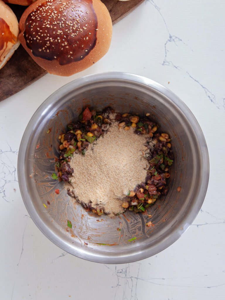 A mixing bowl with the black bean burger mixture and breadcrumbs just added on top