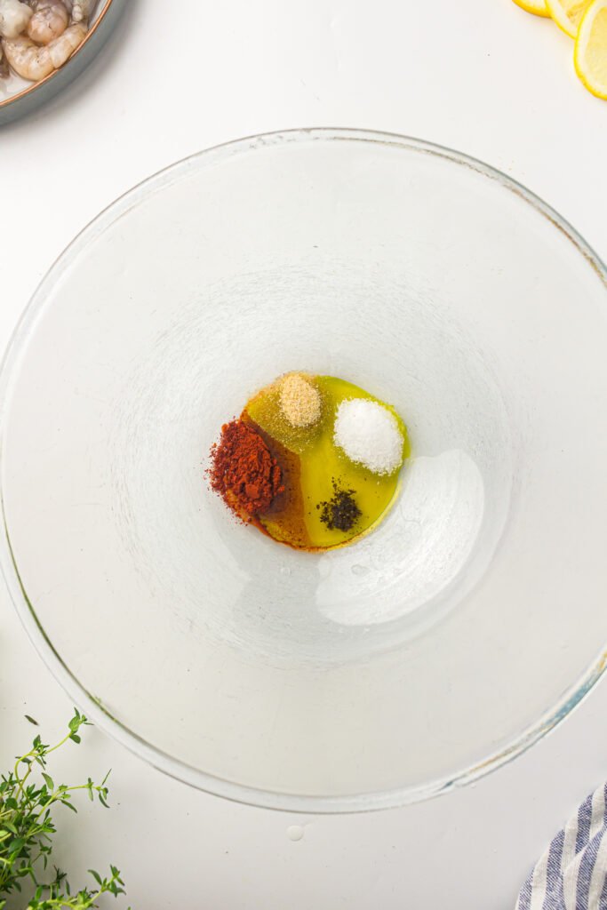 A glass bowl with avocado oil, garlic powder, paprika, salt, and black pepper