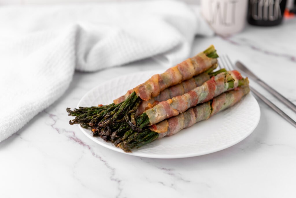 Cooked bacon wrapped asparagus bundles served on a white plate