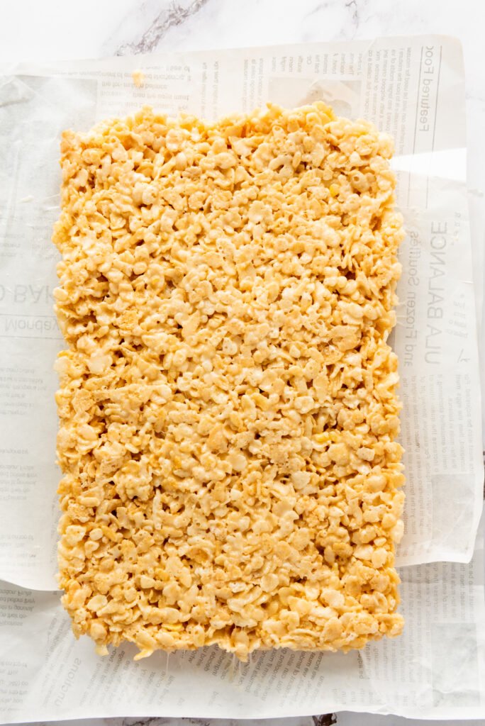 Rice Krispie treat slab lifted out of the dish and placed on parchment paper, ready to be cut into squares