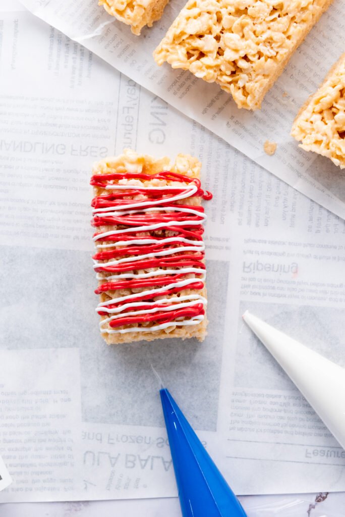 4th of July Rice Krispie treat with red and white drizzle layered across the top, midway through decorating with a piping bag