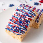 Two 4th of July Rice Krispie treats decorated with red, white, and blue drizzle and sprinkles