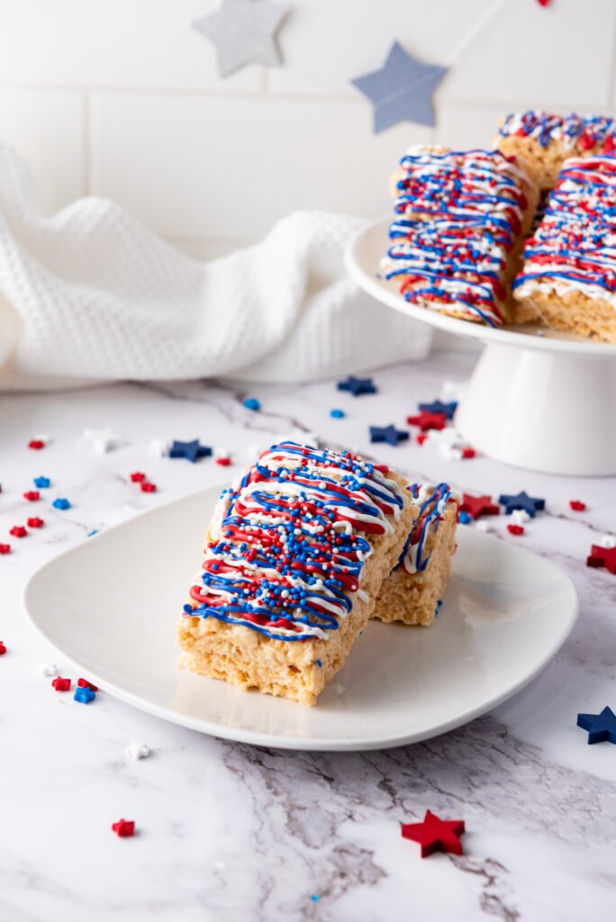 Two 4th of July Rice Krispie treats decorated with red, white, and blue drizzle and sprinkles