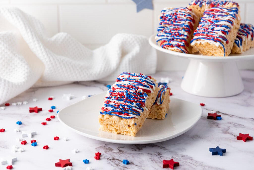 Patriotic Rice Krispie treats with red, white, and blue drizzle served on a white plate