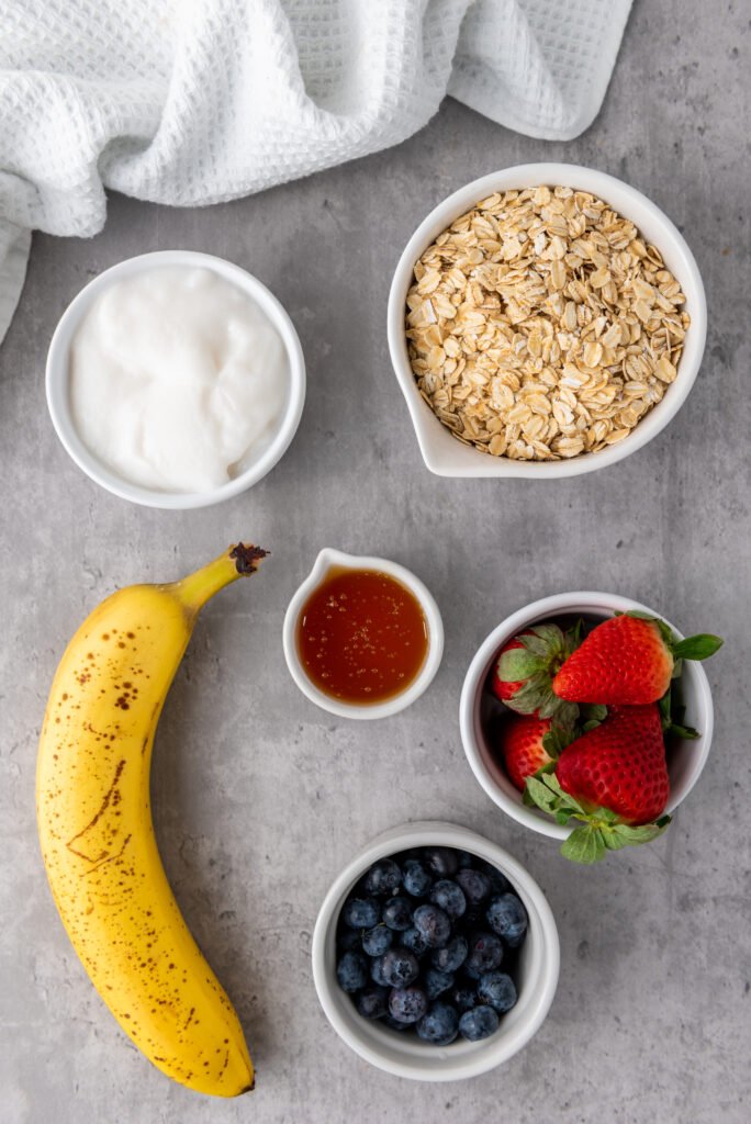 Ingredients for berry granola cups, oats, banana, yogurt, honey, strawberries, and blueberries