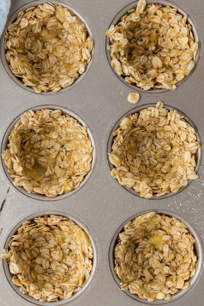 Granola mixture pressed into a muffin pan, ready to be baked into cups