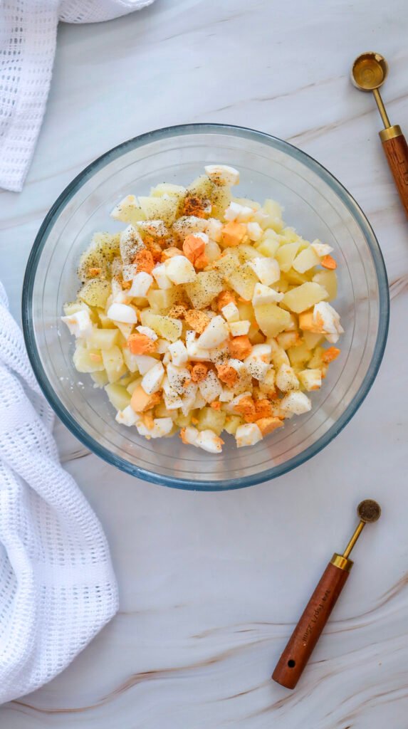 Chopped boiled potatoes and eggs in a glass bowl, sprinkled with black pepper