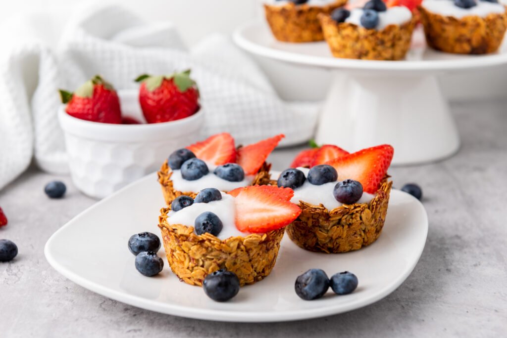 Granola cups topped with yogurt, strawberries, and blueberries on a white plate, with fresh berries scattered around
