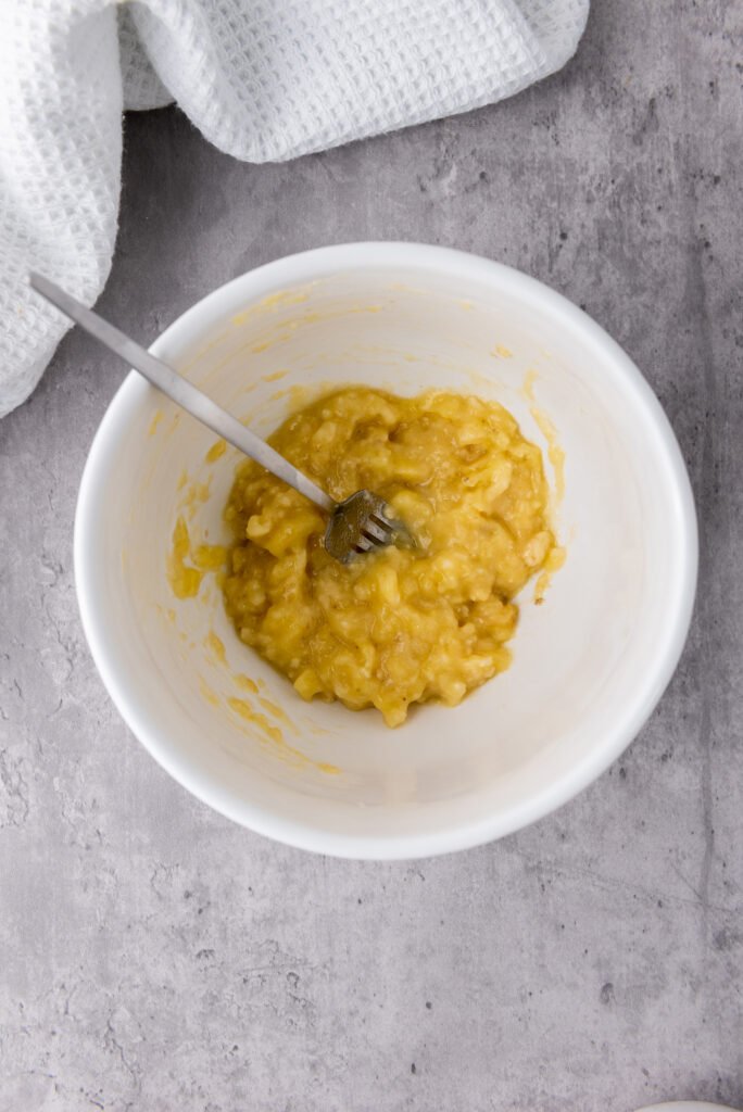 mashed banana in a white bowl with a fork