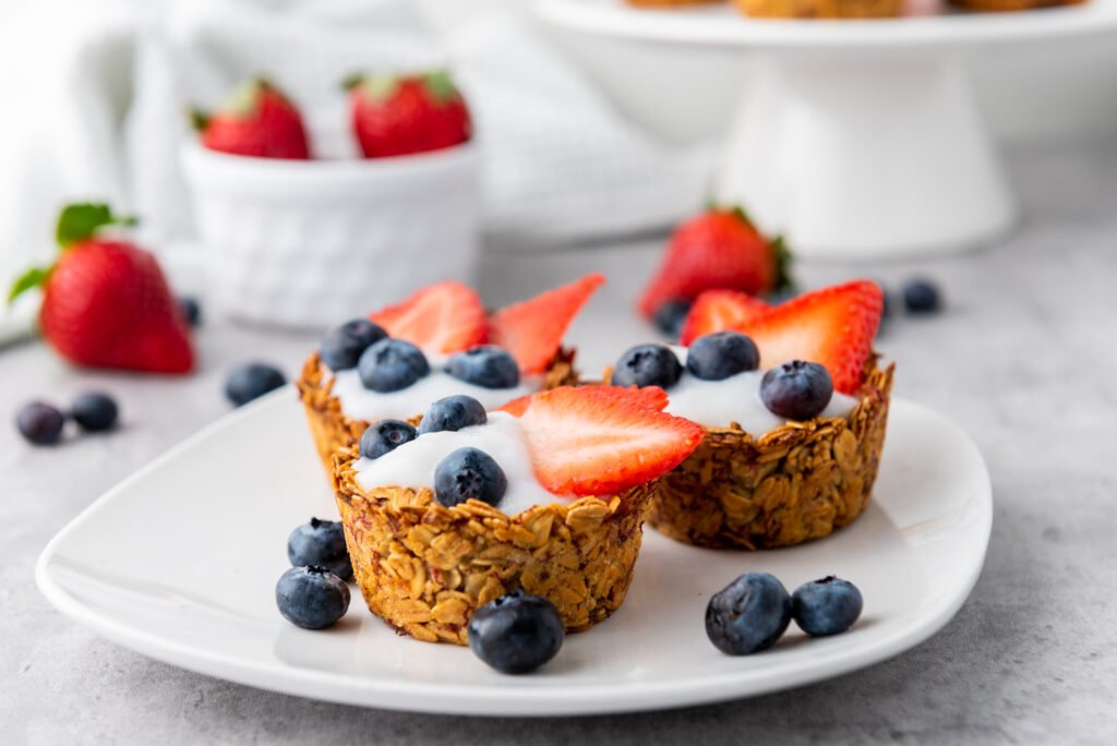 Three granola cups filled with yogurt and topped with sliced strawberries and blueberries on a white plate