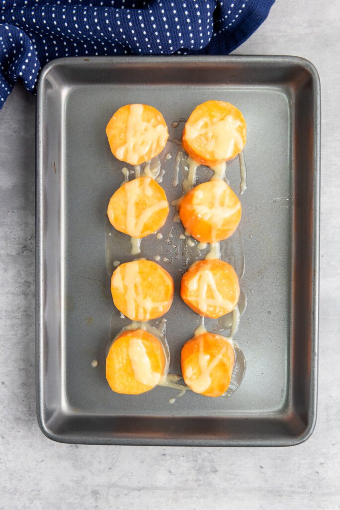 Raw sweet potato slices on a baking tray, drizzled with melted butter