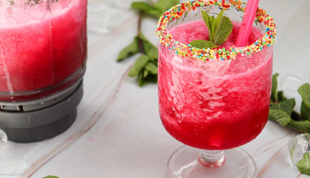 Watermelon slushie served in a sprinkle-rimmed glass with mint and a pink straw