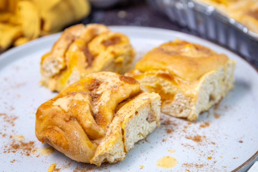 Close-up of three pumpkin cinnamon rolls on a plate, topped with frosting and sprinkled with cinnamon