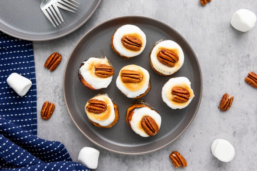 Toasted sweet potato bites topped with golden marshmallows and pecans on a gray plate