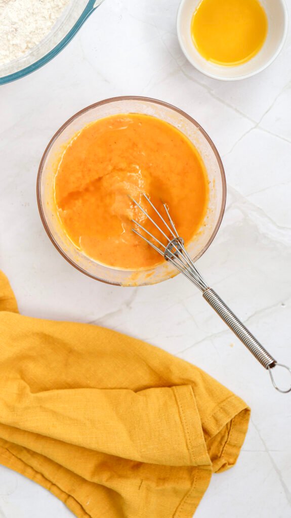 Whisk resting in a bowl of fully combined wet ingredients for pumpkin pancakes