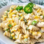 A close-up of creamy Mexican street corn pasta salad in a white bowl, made with rotini, corn, green onions, jalapeños, and cotija cheese