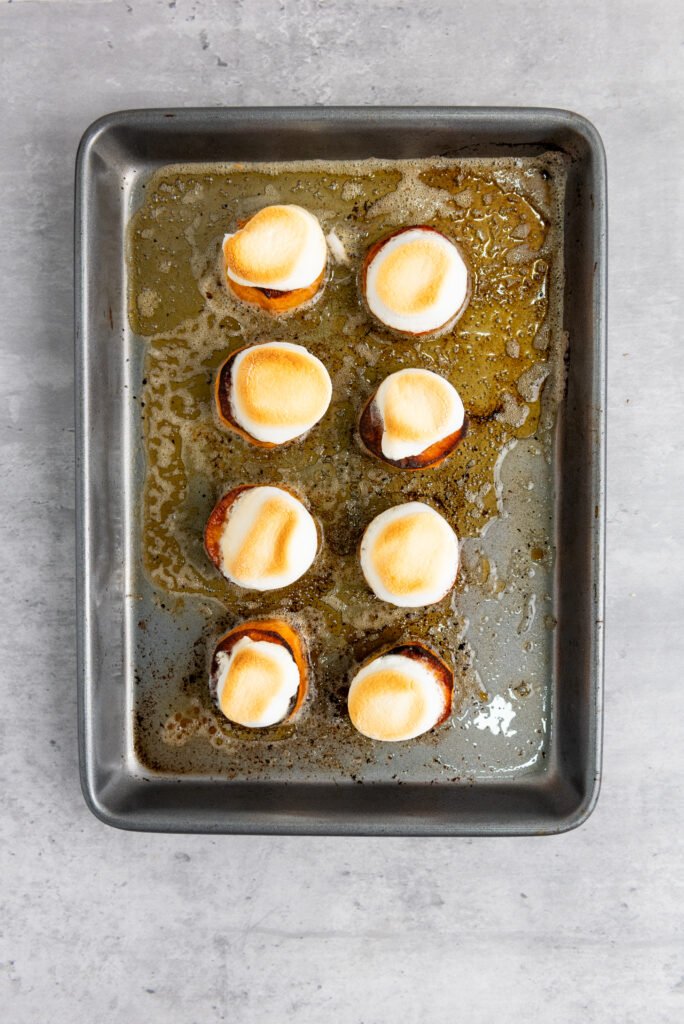 Broiled sweet potato slices on a baking tray, each topped with a golden toasted marshmallow