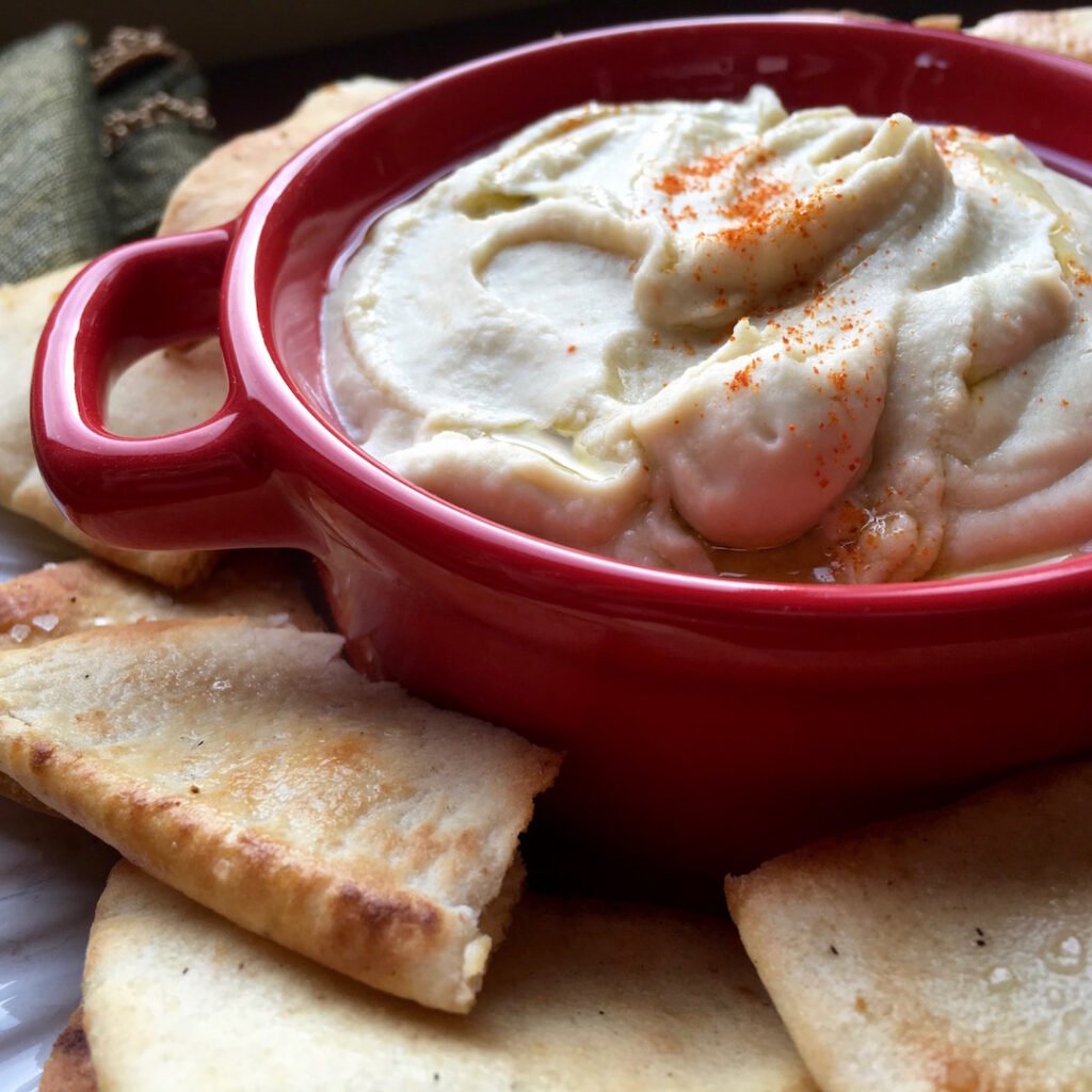 Creamy white bean dip in a red bowl, drizzled with olive oil and sprinkled with cayenne pepper