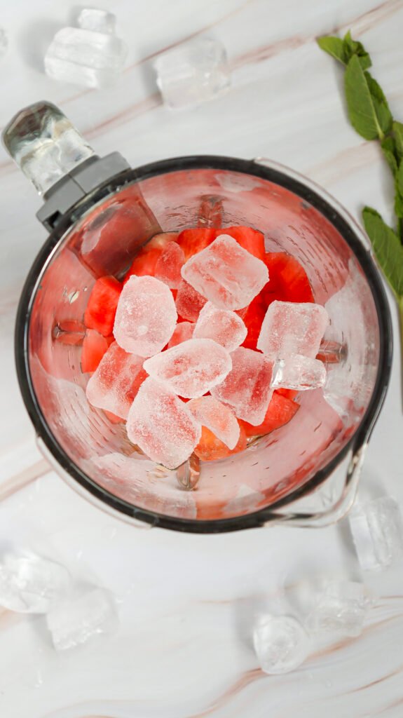 Ice cubes added to a blender with watermelon chunks