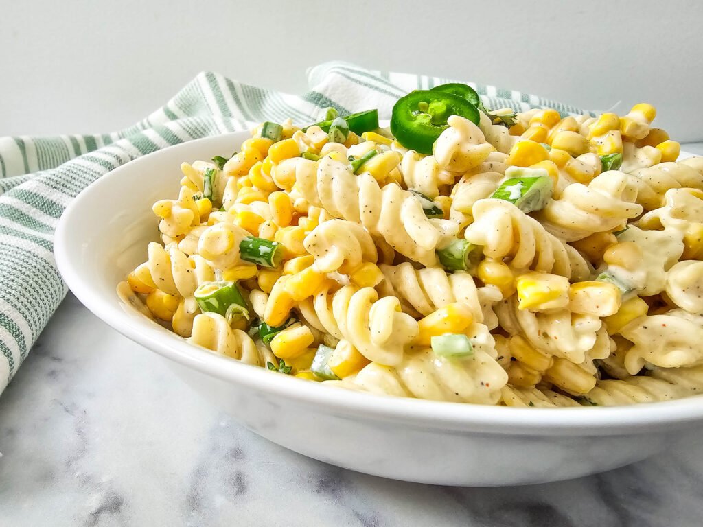Close-up of creamy Mexican street corn pasta salad topped with sliced jalapeños
