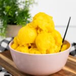 A pink bowl filled with scoops of bright yellow no-churn vegan mango sorbet