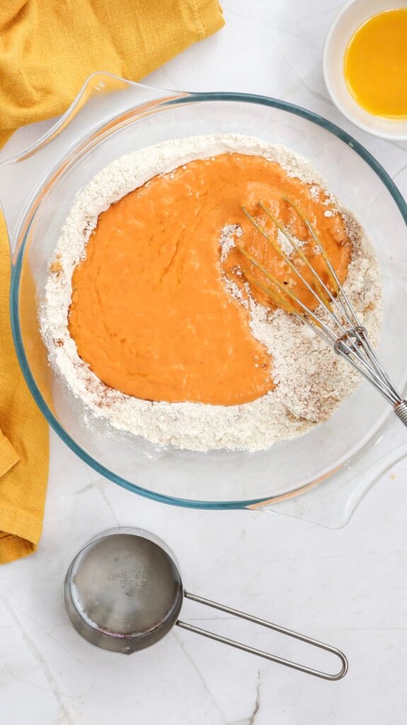 Pumpkin pancake batter wet ingredients poured over the dry mixture in a glass bowl