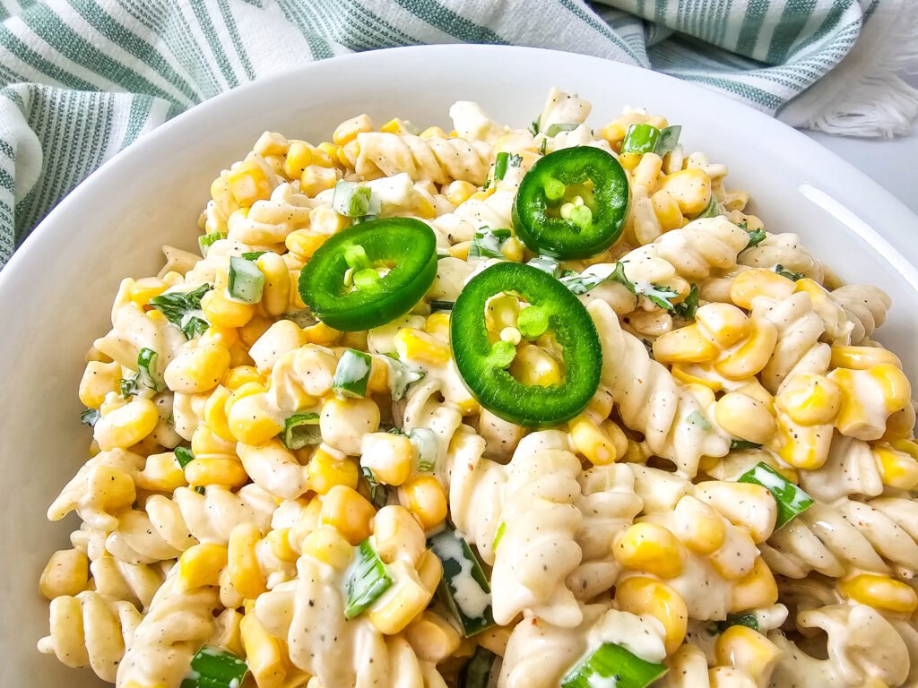 Close-up of creamy Mexican street corn pasta salad topped with sliced jalapeños
