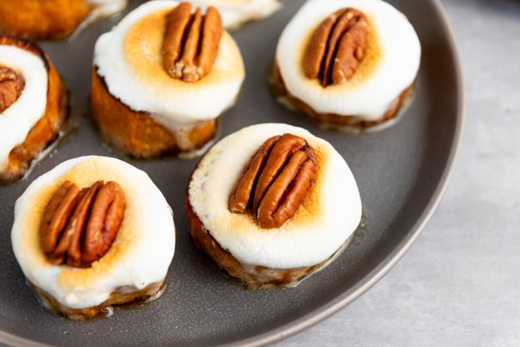 Toasted sweet potato bites topped with golden marshmallows and pecan halves on a gray plate