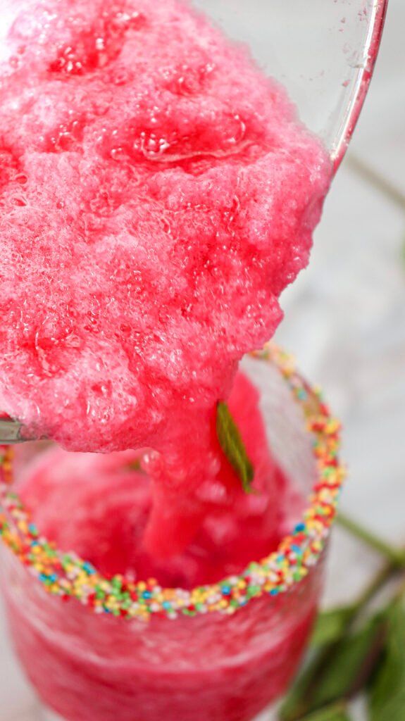 Pouring blended watermelon slushie into a glass with a sprinkle-coated rim