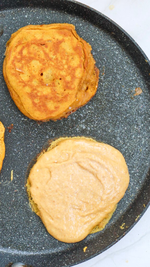 Pumpkin pancake batter cooking on a skillet, with one pancake flipped and golden brown while another is still raw