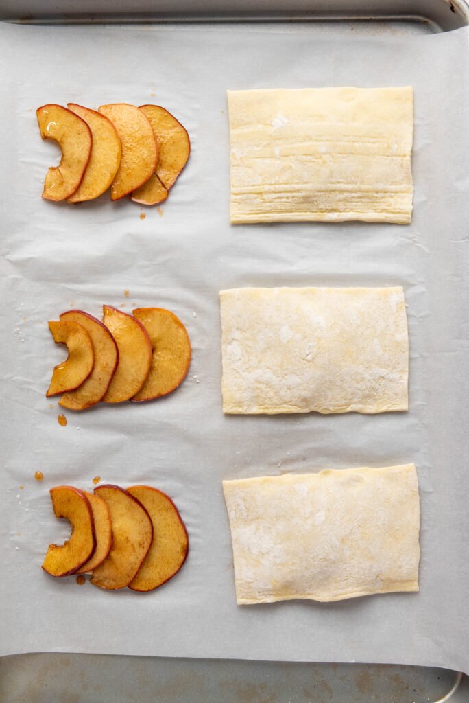 Caramelized apple slices topped with puff pastry rectangles on a baking sheet