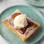 Upside down apple tart topped with a scoop of vanilla ice cream and dusted with powdered sugar on a light green plate