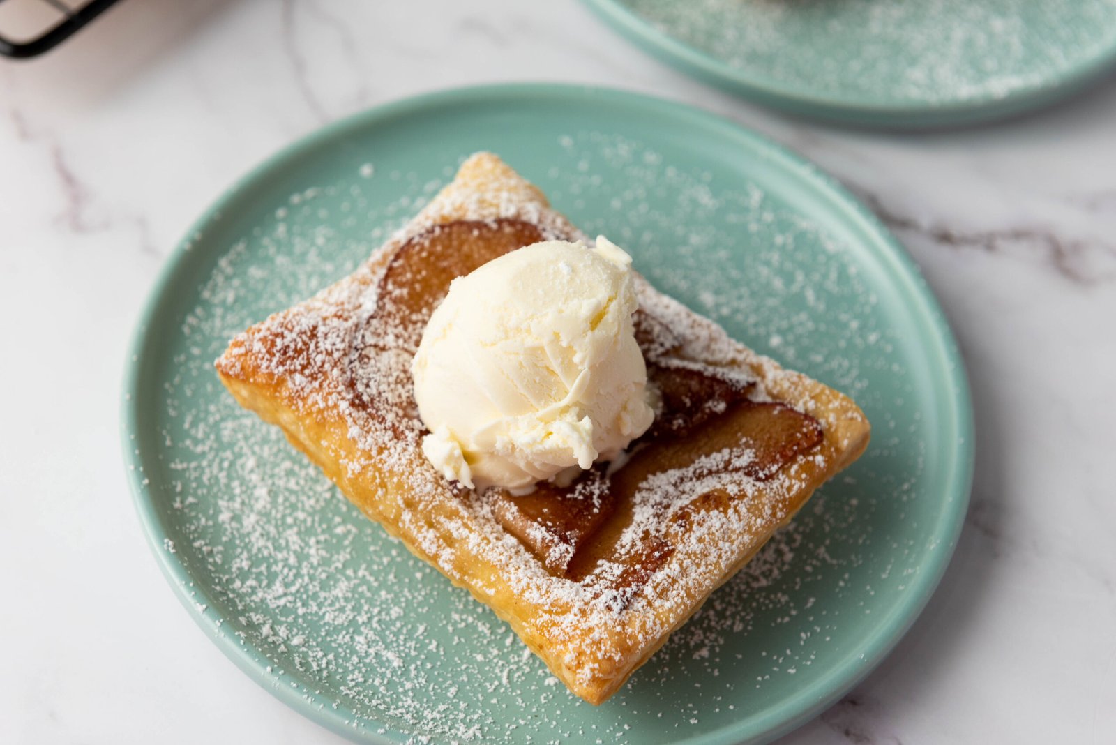 Upside down apple tart topped with a scoop of vanilla ice cream and dusted with powdered sugar on a light green plate