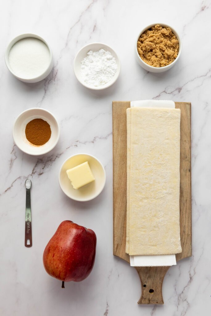 Ingredients for upside down apple tarts including puff pastry, apple, butter, sugars, cinnamon, salt, and confectioners’ sugar