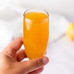 A hand holding a champagne flute filled with golden apple cider mimosa