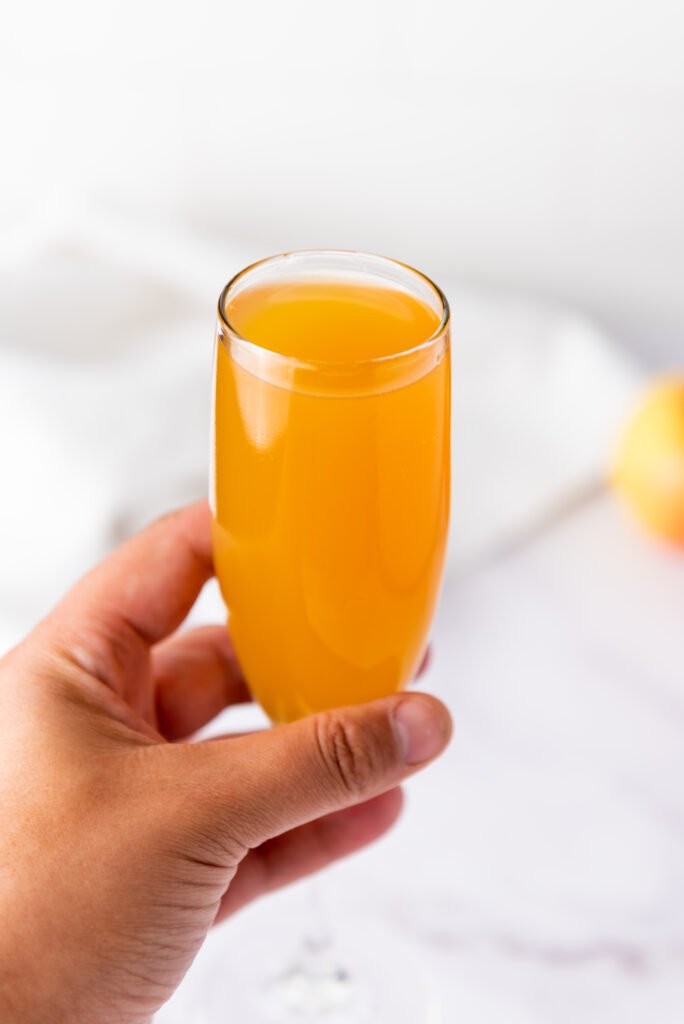 A hand holding a champagne flute filled with golden apple cider mimosa
