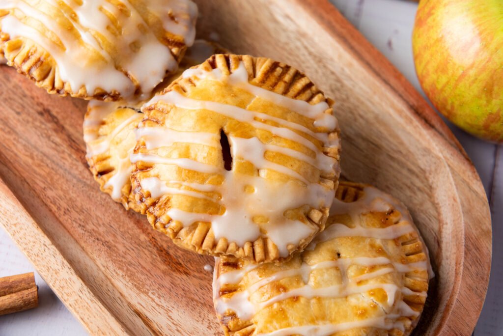apple hand pies drizzled with sweet glaze, served on a wooden tray with fresh apples and cinnamon sticks nearby