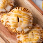 apple hand pies drizzled with sweet glaze, served on a wooden tray with fresh apples and cinnamon sticks nearby