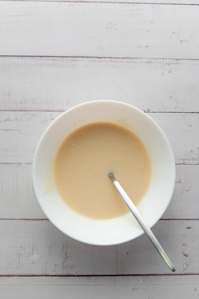 Smooth vanilla glaze in a white bowl with a spoon, ready to drizzle over baked apple hand pies