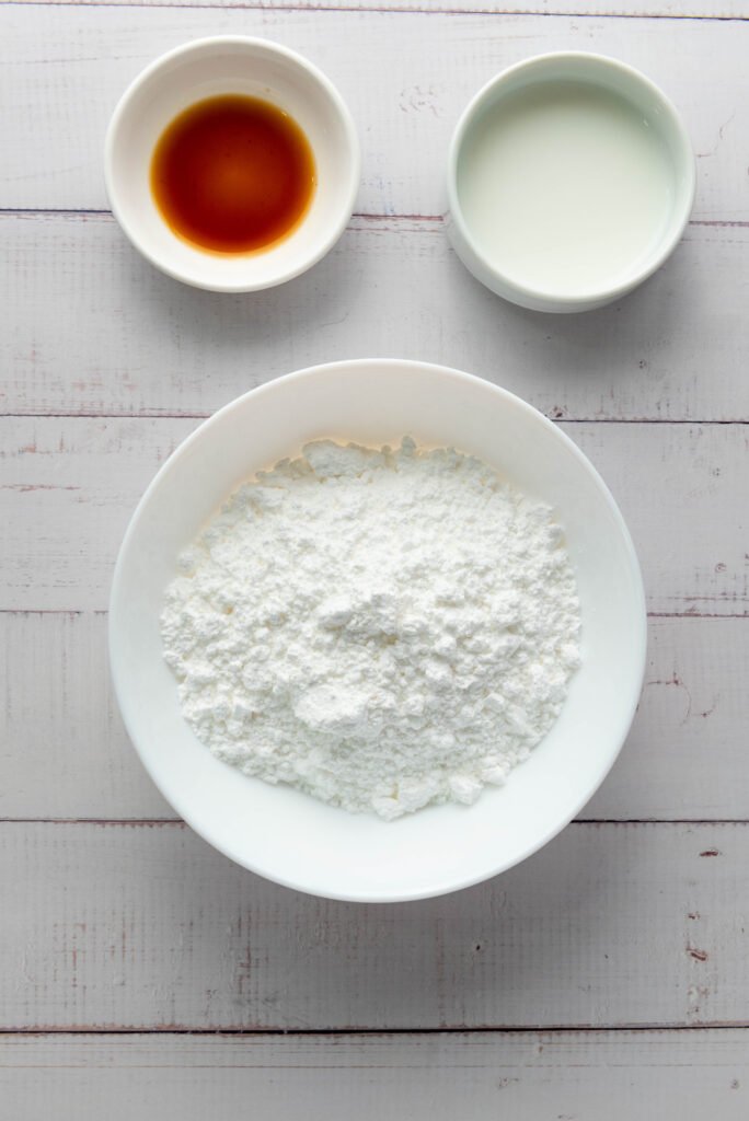 Powdered sugar in a bowl with small bowls of milk and vanilla extract, ready to make glaze for apple hand pies