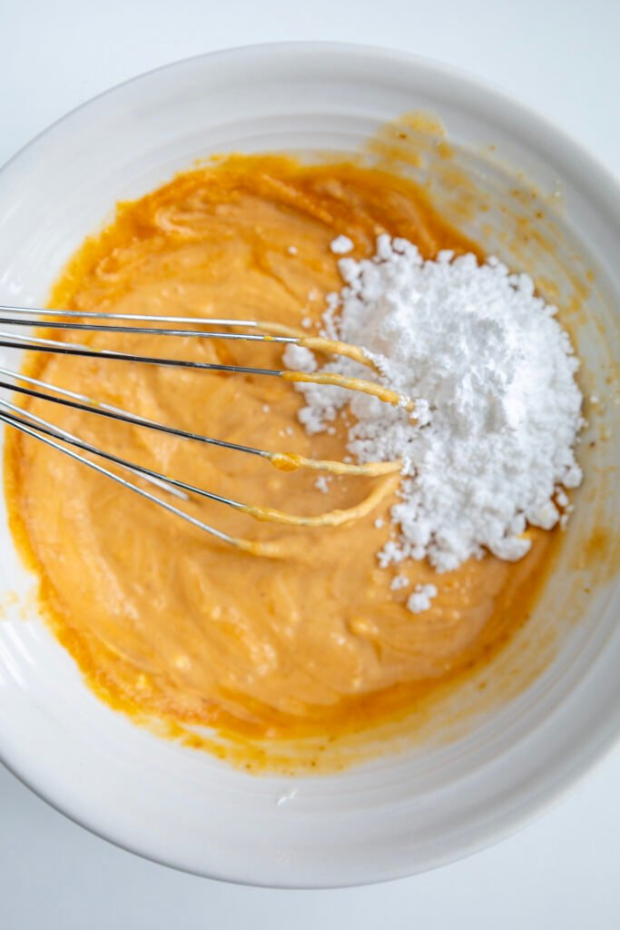 Adding powdered sugar to pumpkin mixture while whisking the frosting