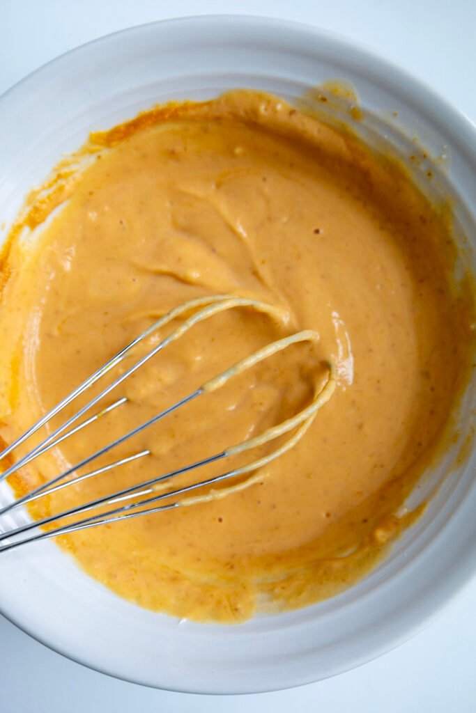 Whisking together pumpkin puree, cream cheese, powdered sugar and lemon juice until smooth and creamy to make pumpkin cinnamon rolls frosting