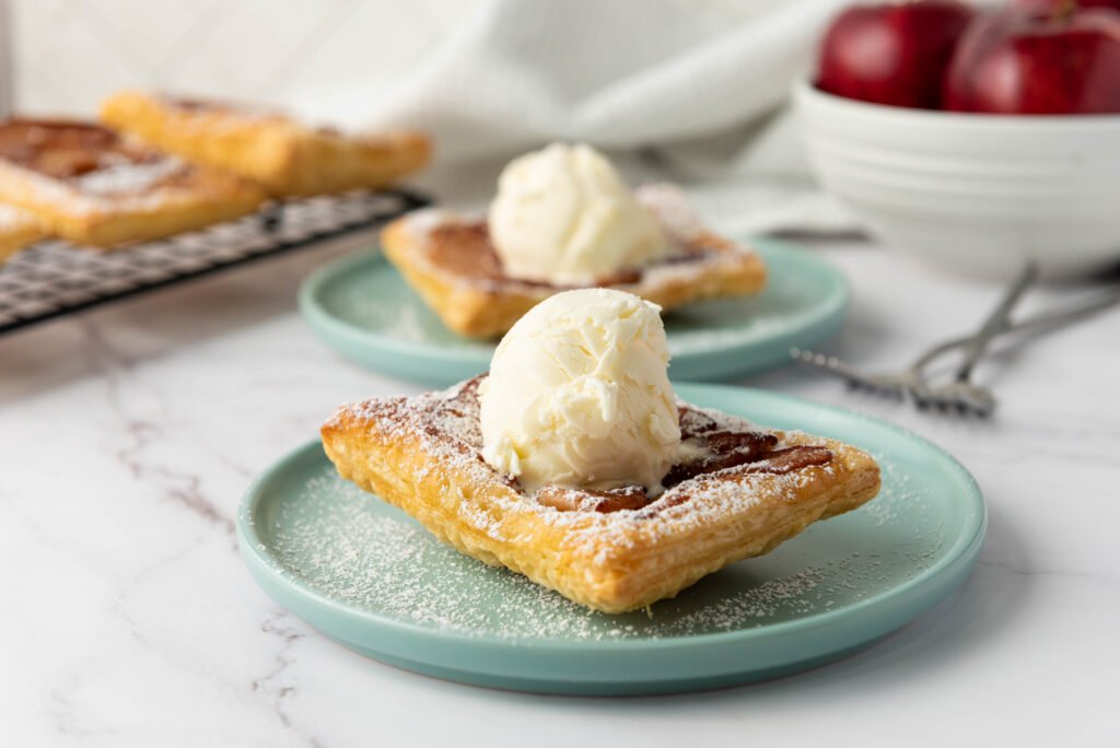 Upside down apple tart served on a plate, topped with a scoop of vanilla ice cream and dusted with powdered sugar