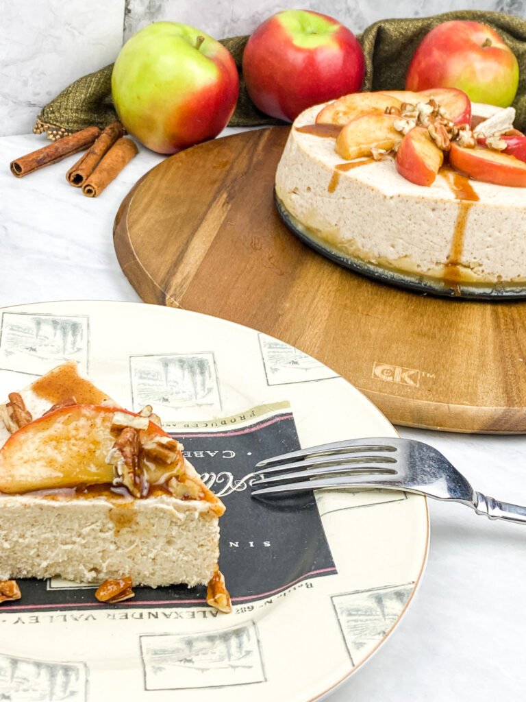 Close-up of a finished apple cinnamon cheesecake topped with apple slices, chopped pecans, and cinnamon-maple drizzle