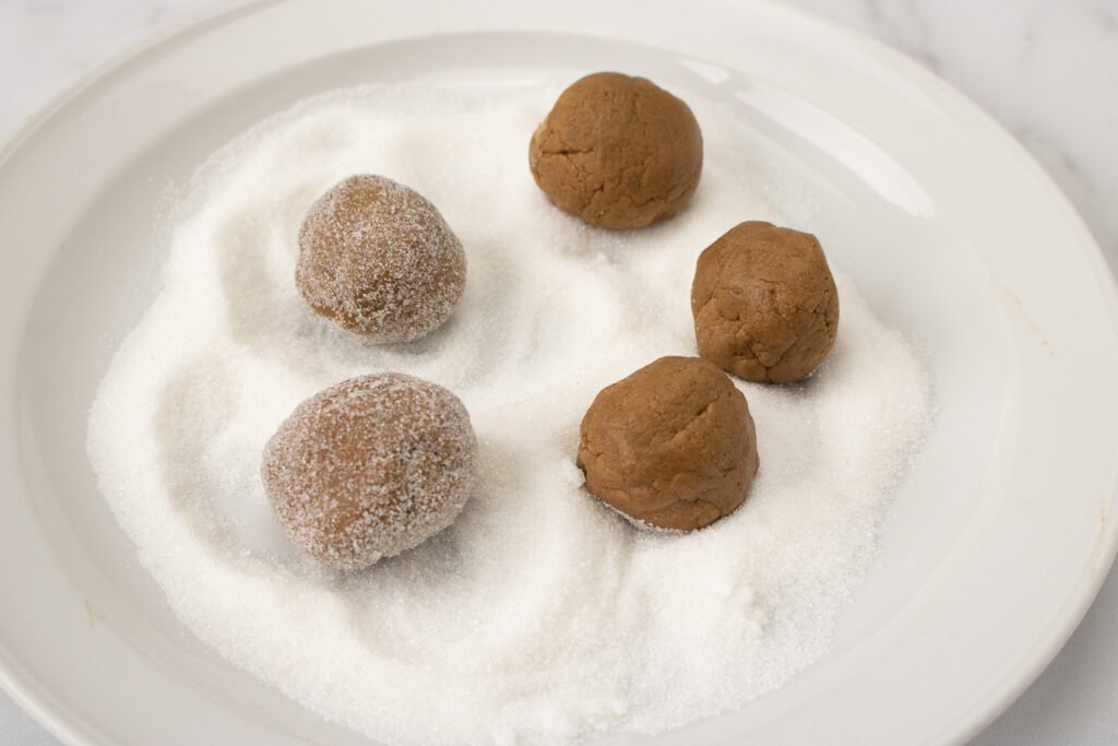 Some cookie dough balls have been rolled in sugar, while others are still uncoated on the plate