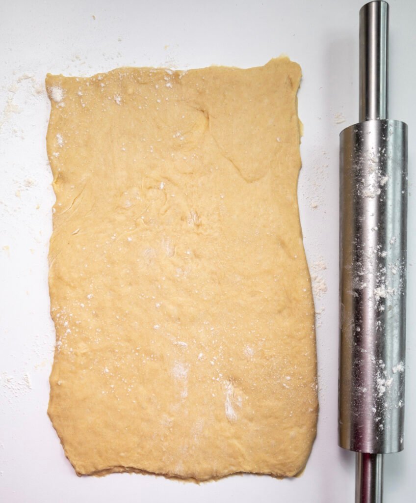 Pumpkin cinnamon roll dough rolled out into a rectangle on a floured surface