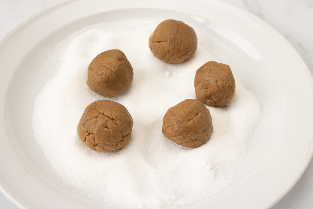 Cookie dough balls placed on a plate of granulated sugar